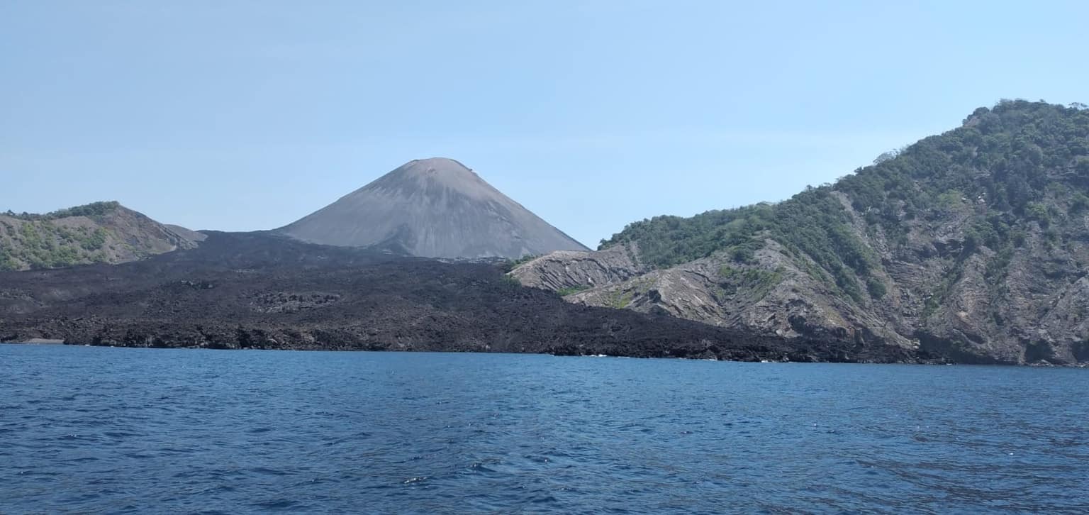 The Barren Island volcanic cone rising from the sea beyond black lava fields, seen from a boat