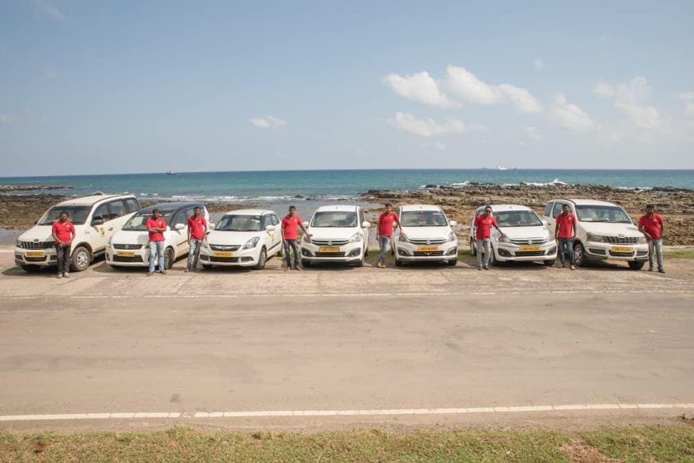 Tropical Andamans drivers standing with the company's fleet of white taxis by the sea in Port Blair